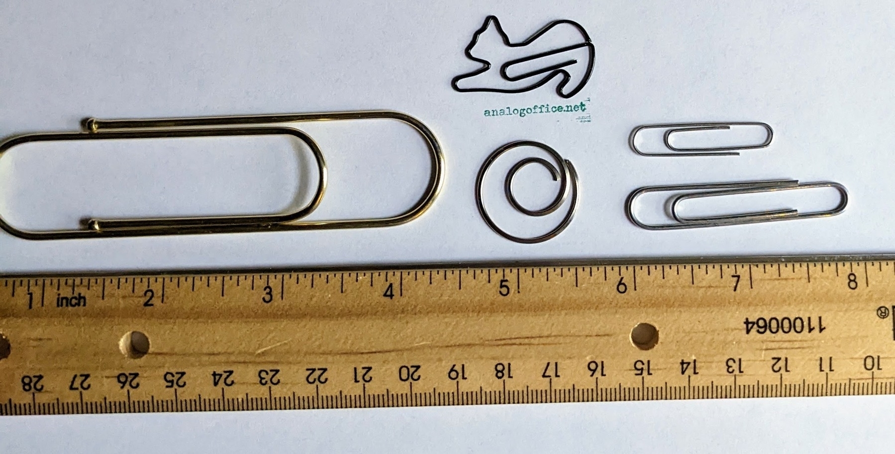 a large novelty paper clip next to a spiral-shaped paper clip, a paper clip shaped like a cat, and a small and large normal paper clip