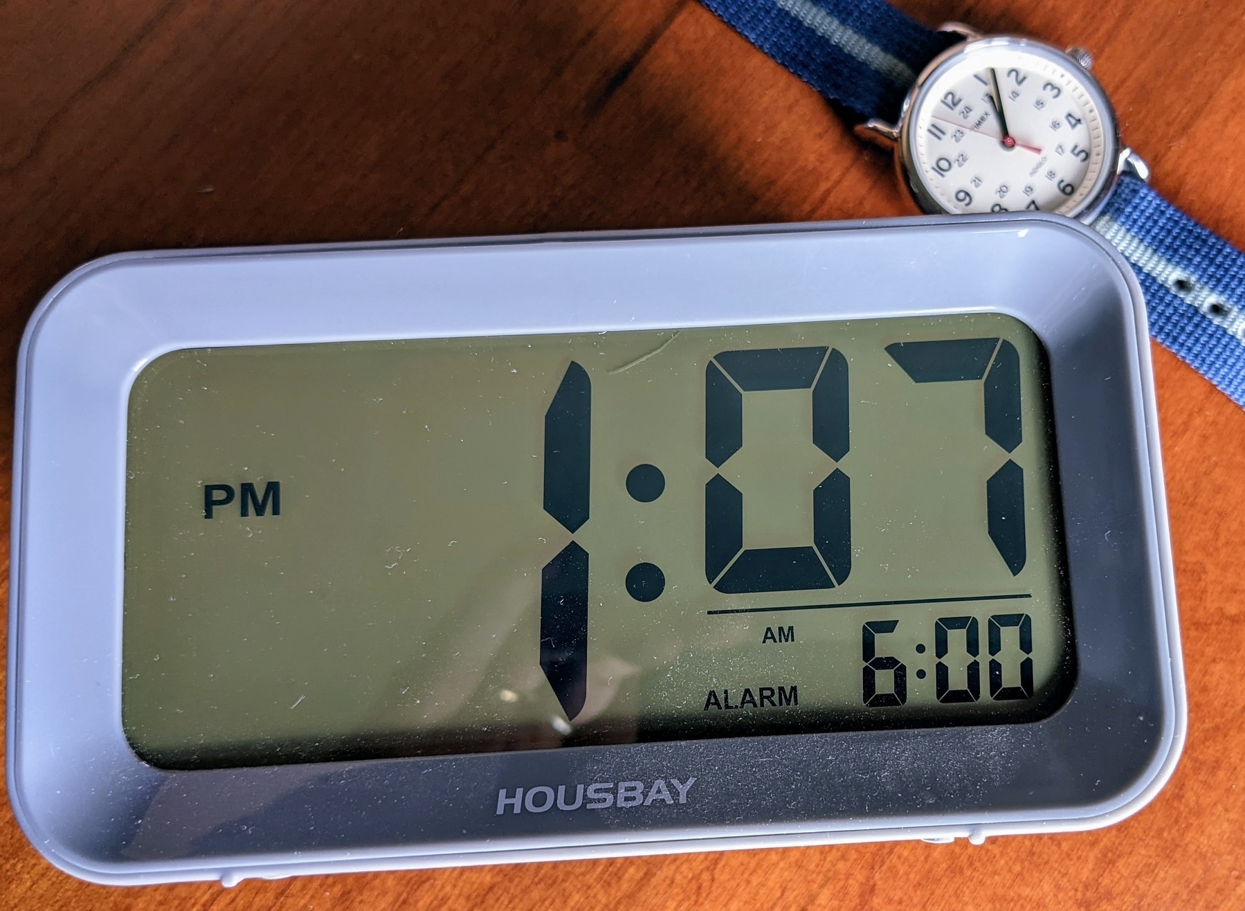 a digital bedside alarm clock next to a Timex wrist watch